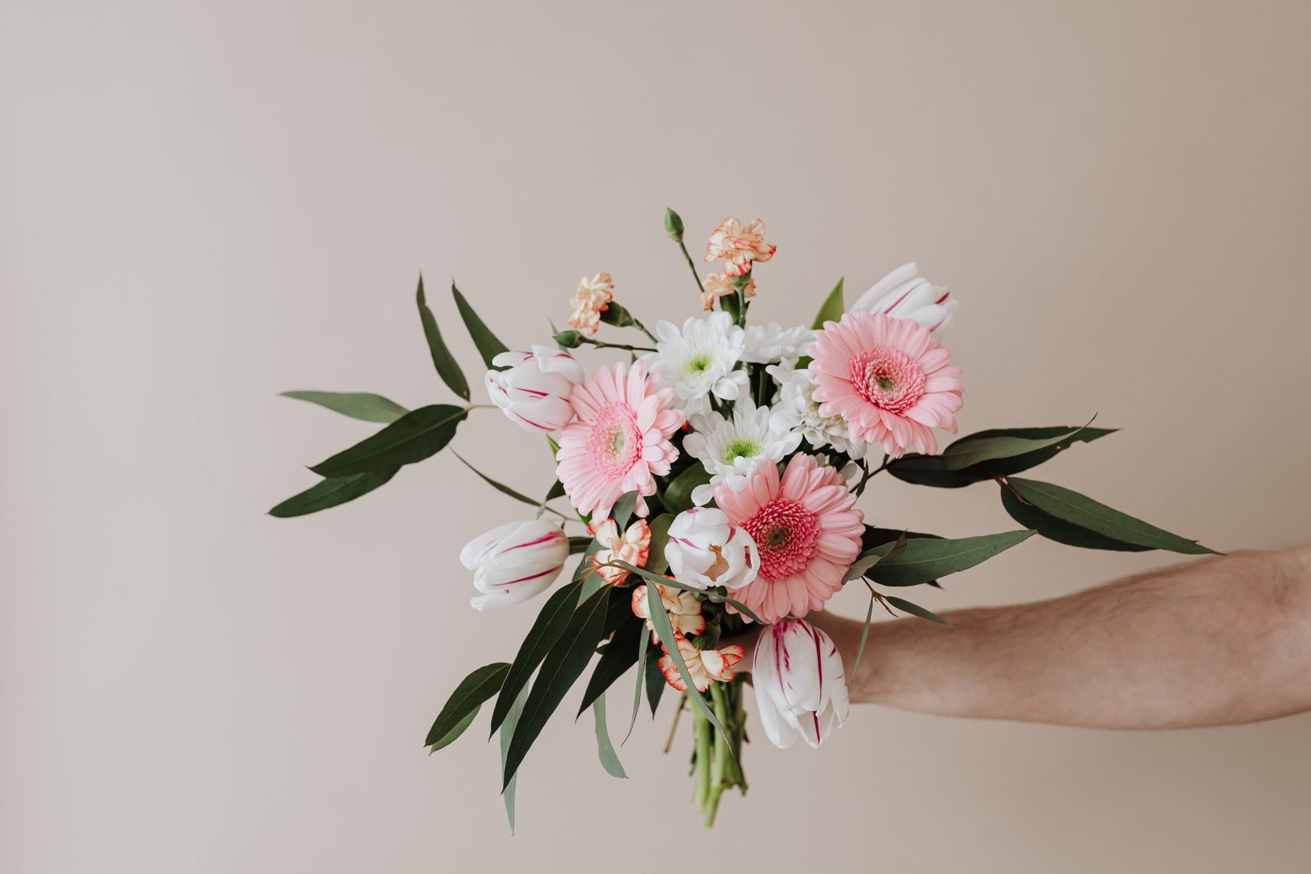 Crop florist holding bouquet of flowers in hand near beige wall
